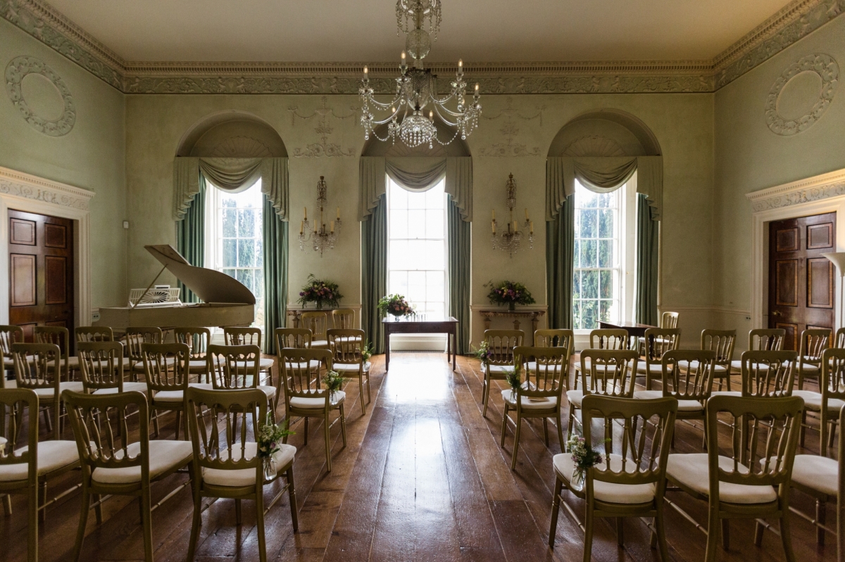 The Saloon set up for a wedding ceremony facing the windows, with views over the lake and the countryside beyond.